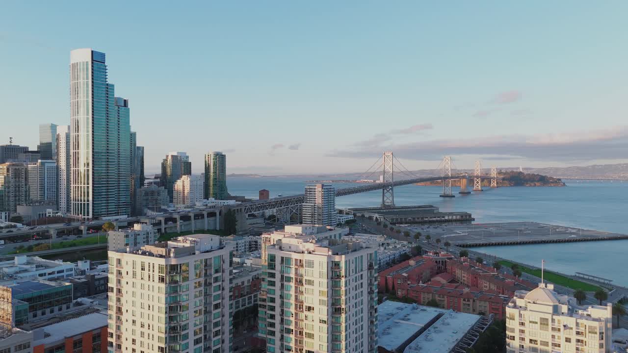 Drone captures the San Francisco–Oakland Bay Bridge with downtown high-rise buildings and the U.S. 101 (James Lick Bayshore Freeway) in the foreground, showcasing the urban skyline