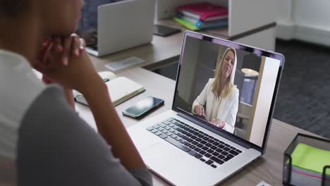 mujer de negocios afroamericana sentada en un escritorio usando una computadora portátil haciendo una videollamada con una colega