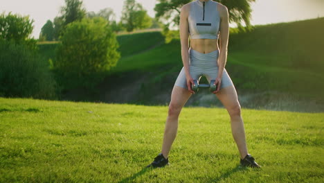 strong sportswoman performs exercises for muscles of thighs and buttocks outdoors