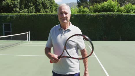 portrait of smiling senior caucasian man holding tennis racquet on tennis court on sunny day