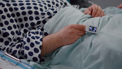 closeup of sick man patient resting in bed with medical oximeter on finger