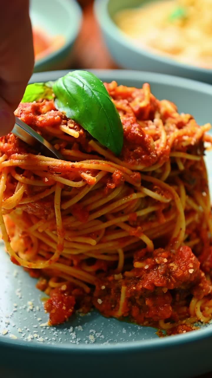 Spaghetti con ragù di carne al pomodoro e foglia di basilico fresco. Primo piano di un piatto di pasta italiana con sugo rosso e carne macinata, guarnito con basilico verde su un piatto blu.