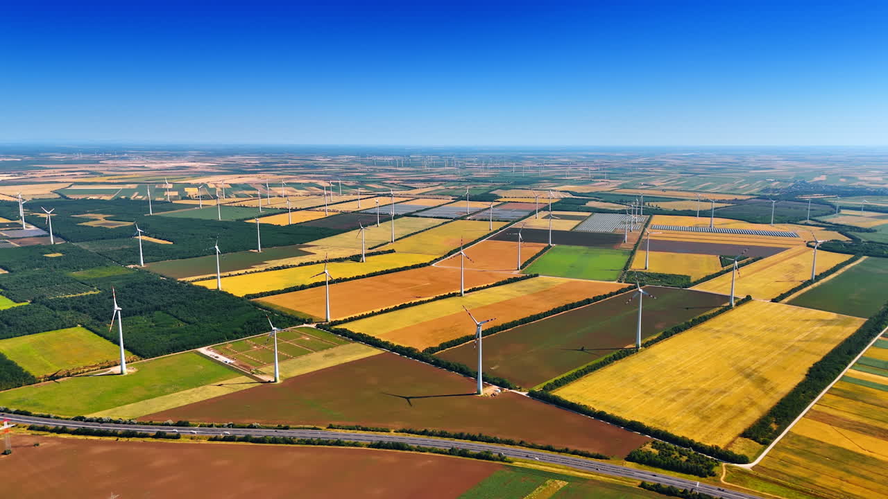 Flight over the rural landscape divided into colorful fields. Multiple wind mills produce green energy in the countryside