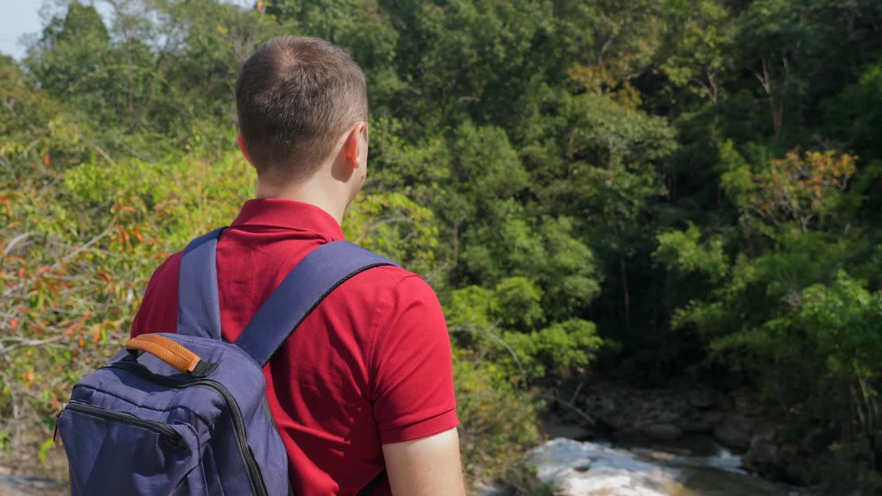 vista trasera de un hombre de viaje con una mochila de pie en la roca y mirando al río