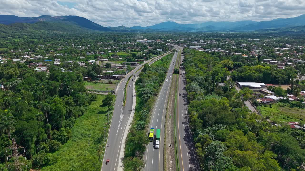 Cars driving along Autopista Duarte highway, city of Bonao, and beautiful mountain landscape, Dominican Republic. Aerial forward