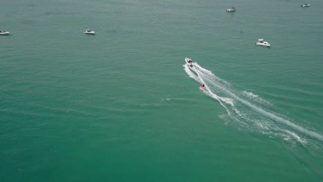 tracking aerial: man on red surfboard waterskies on green lagoon water