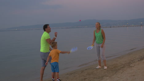 niño y padres jugando al tenis en la playa