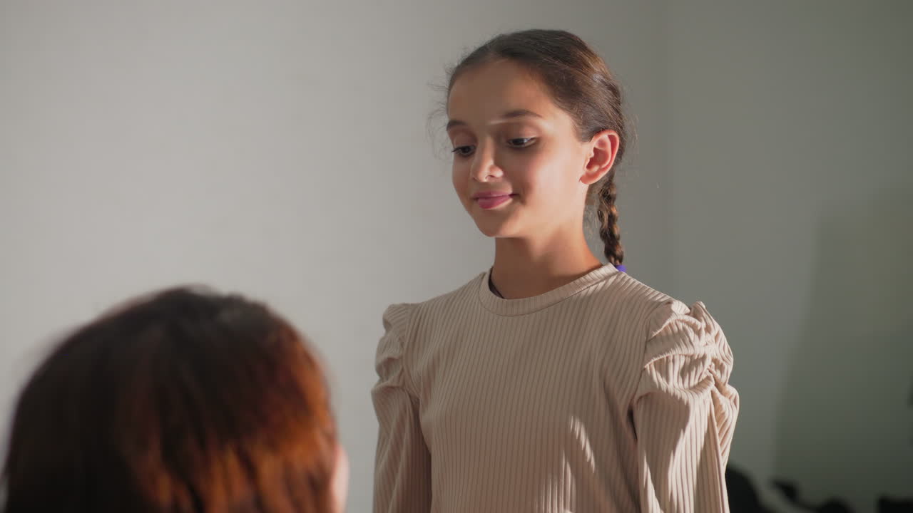 mum adjusting daughter’s braided pigtails on sofa closeup of caring hands smoothing hair and fabric child standing relaxed in sunlit living room intimate mother child bonding moment warm cozy home atmosphere