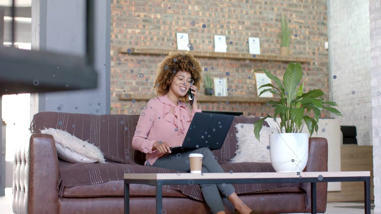 Woman holding phone, using laptop doing remote work, camera pulling back revealing coffee cup plant