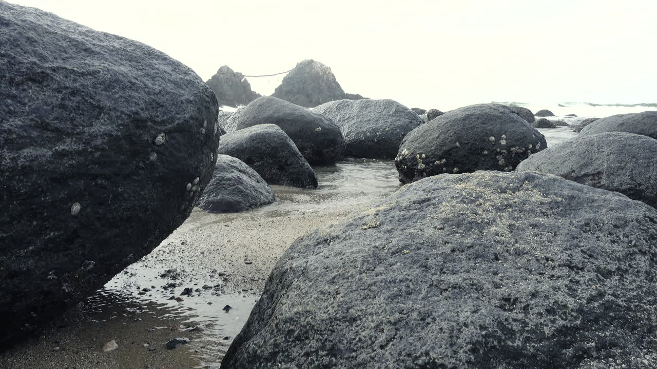 Sea   water getting between rocks reaching the sand on the shore of a beach with the ocean and a mountain background close up shot