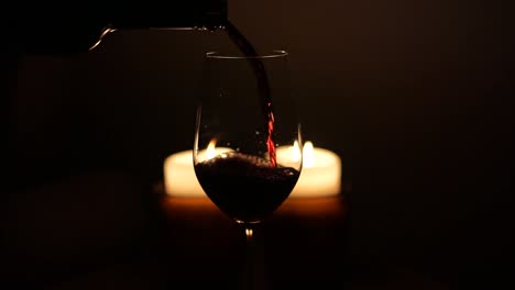 a glass of red wine in front of two burning candles