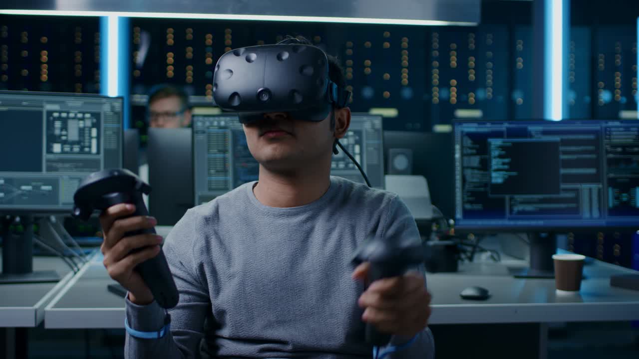 Portrait of Software Delevoper Wearing Virtual Reality Headset Using Controllers to Develop and Program VR Gaming and Applications. In the Background Technology Developing Studio with Computers and Monitors