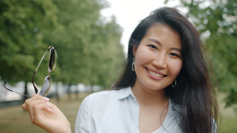smiling asian woman wearing sunglasses in a park
