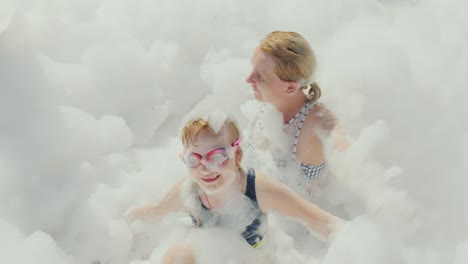 a foam party in a resort hotel on the beach, a young mother with her daughter having fun in a huge amount of foam