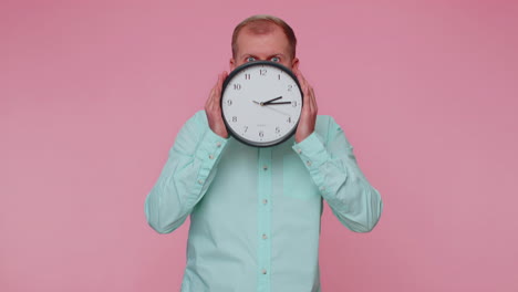 Young-man-holding-clock-watch,-hiding,-checking-time-on-clock,-running-late-to-work-being-in-delay