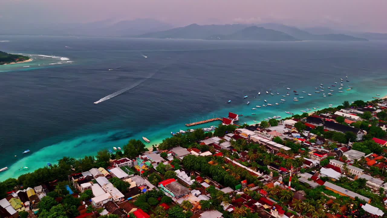 Gili Trawangan township and coast with moving vessel, aerial panoramic view