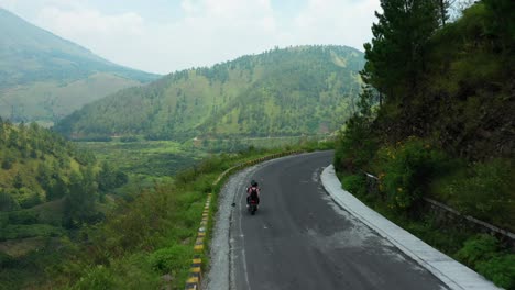 aerial drone tracker footage of two scooter riders on a ride through cliffs overlooking lake toba in north sumatra, indonesia