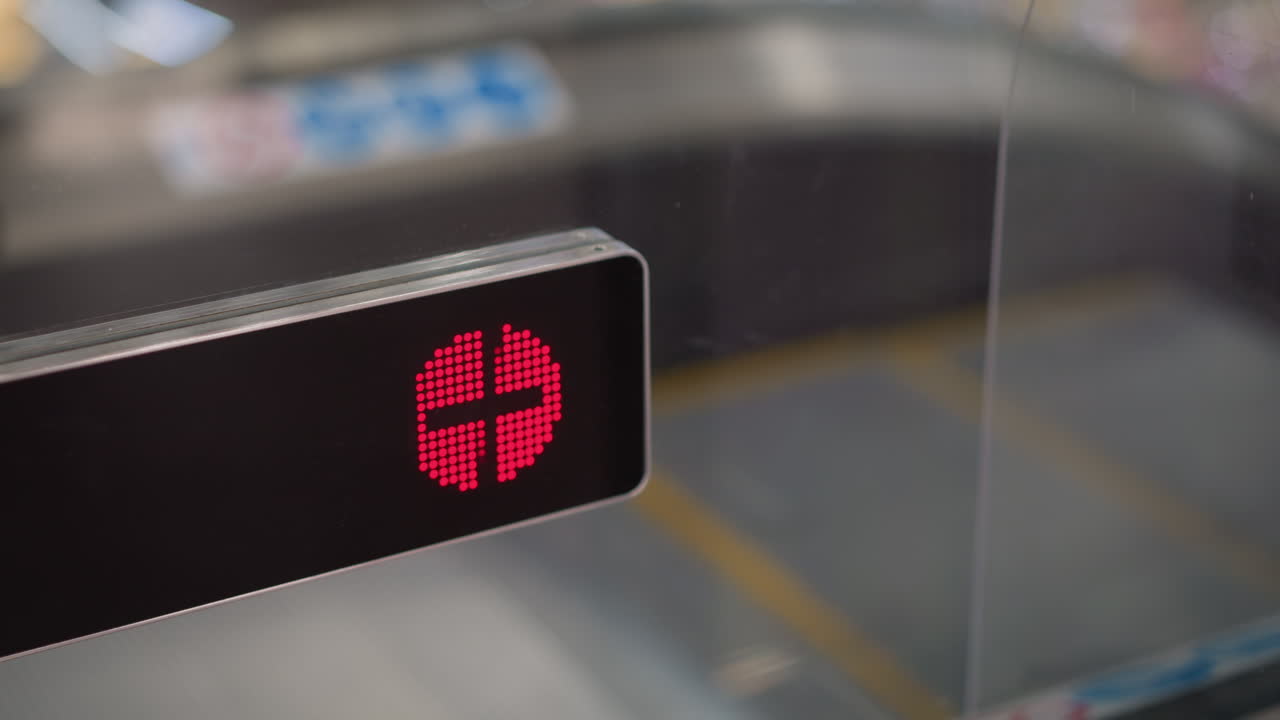 close up red warning indicator blinking on moving walkway entrance glass barrier signaling stop as escalator steps move beneath reflective mall lighting and shoppers blur beyond transparent panel