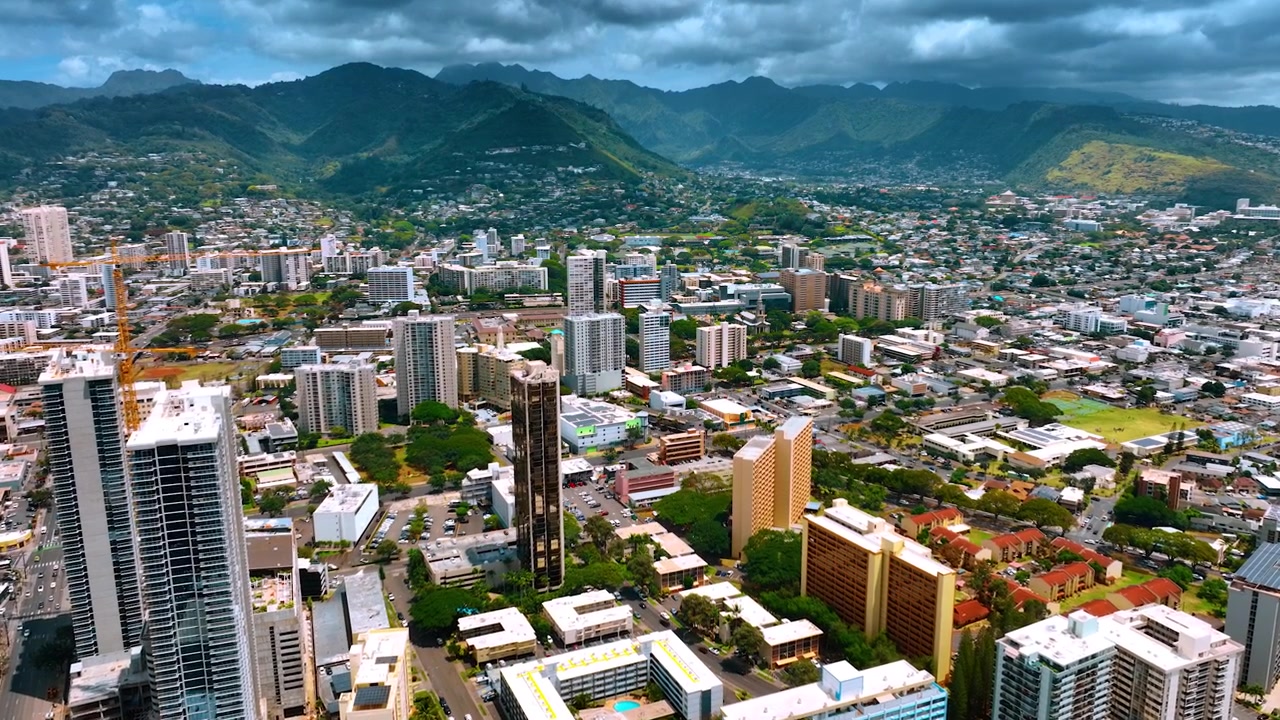 Panorama della moderna e bellissima Honolulu, Hawaii. Le montagne verdeggianti che circondano la città sono coperte da un cielo nuvoloso scuro. Ripresa aerea