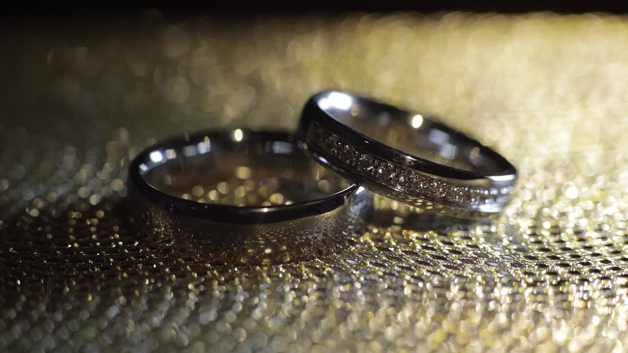 Wedding rings lying, rotate, spinning on shiny golden shining surface with light, close-up macro