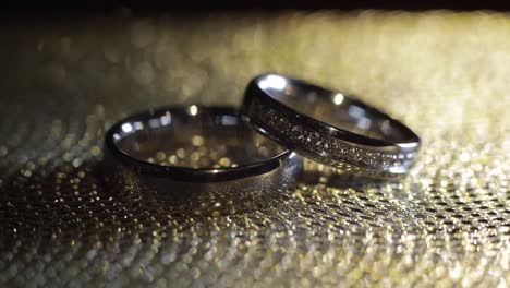 Wedding-rings-lying,-rotate,-spinning-on-shiny-golden-shining-surface-with-light,-close-up-macro