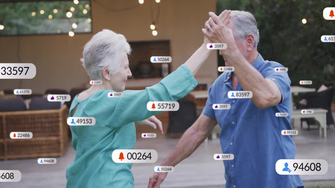 Senior couple dancing on backyard patio, showcasing floating social media marketing alerts