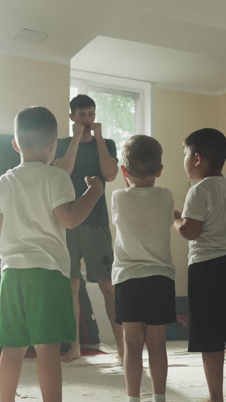 아이들은 무술 수업에서 강사와 함께 공부합니다. 어린 소년들은 체육관에서 느린 동작으로 센세이와 함께 주먹을 맞는 것에서 머리를 보호합니다. 전투 학교