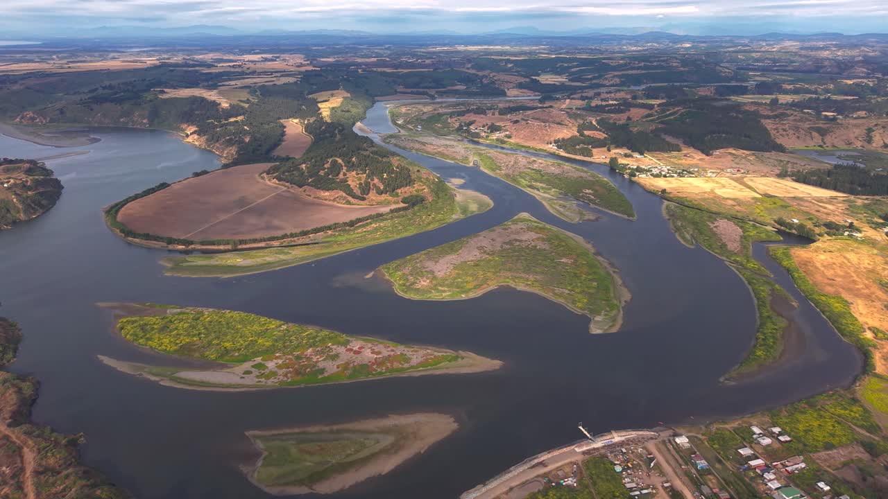 Vista aerea ad alta quota di un estuario fluviale tortuoso con isole verdeggianti e fertili terreni agricoli vicino a un villaggio in Cile, 4K