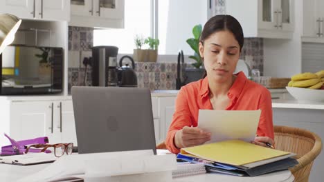 Biracial-woman-using-laptop-and-working-in-kitchen