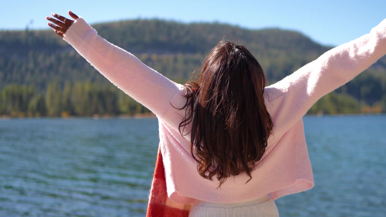 カメラが周囲の荒野の風景に向かって滑らかに移動する中、開放感、自由、そして自然とのつながりを受け入れる女性を捉えたスローモーションの屋外クリップ