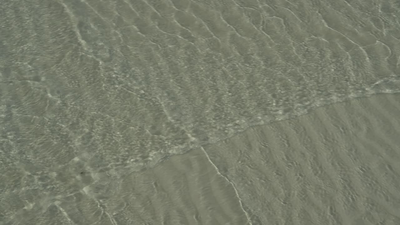 pequeñas olas cruzando en aguas poco profundas de la playa de arena, patrón de ondulación en la arena