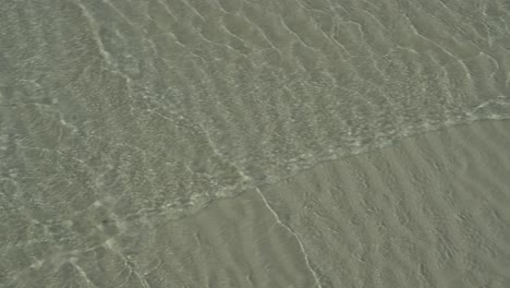 Small-waves-crossing-in-shallows-of-sandy-beach,-ripple-pattern-in-sand