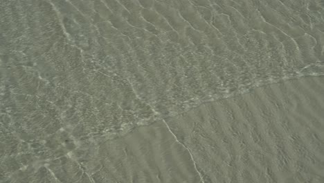 small waves crossing in shallows of sandy beach, ripple pattern in sand