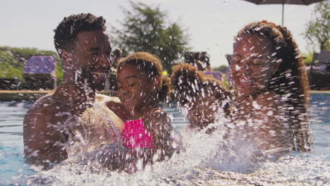 family on summer holiday with two girls being held in swimming pool by parents and splashing