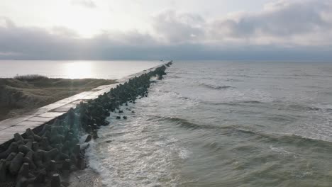 aerial establishing view of port of liepaja concrete pier, baltic sea coastline day, big waves splashing, slow motion birdseye drone shot moving forward