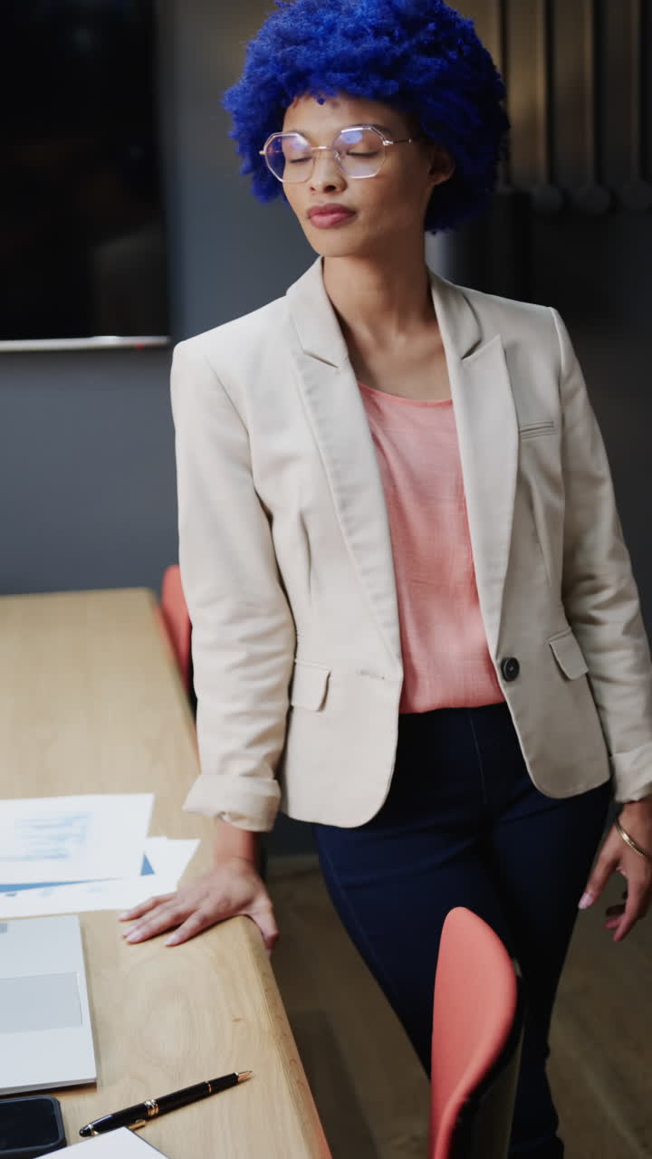 Vertical video of portrait of happy biracial businesswoman with blue afro in office, slow motion