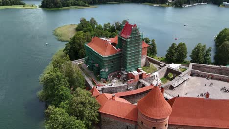 trakai island castle in lithuania, showcasing its red brick walls, towers, and courtyard filled with tourists during a sunny summer day, with lake galvė surrounding , drone orbiting low angle