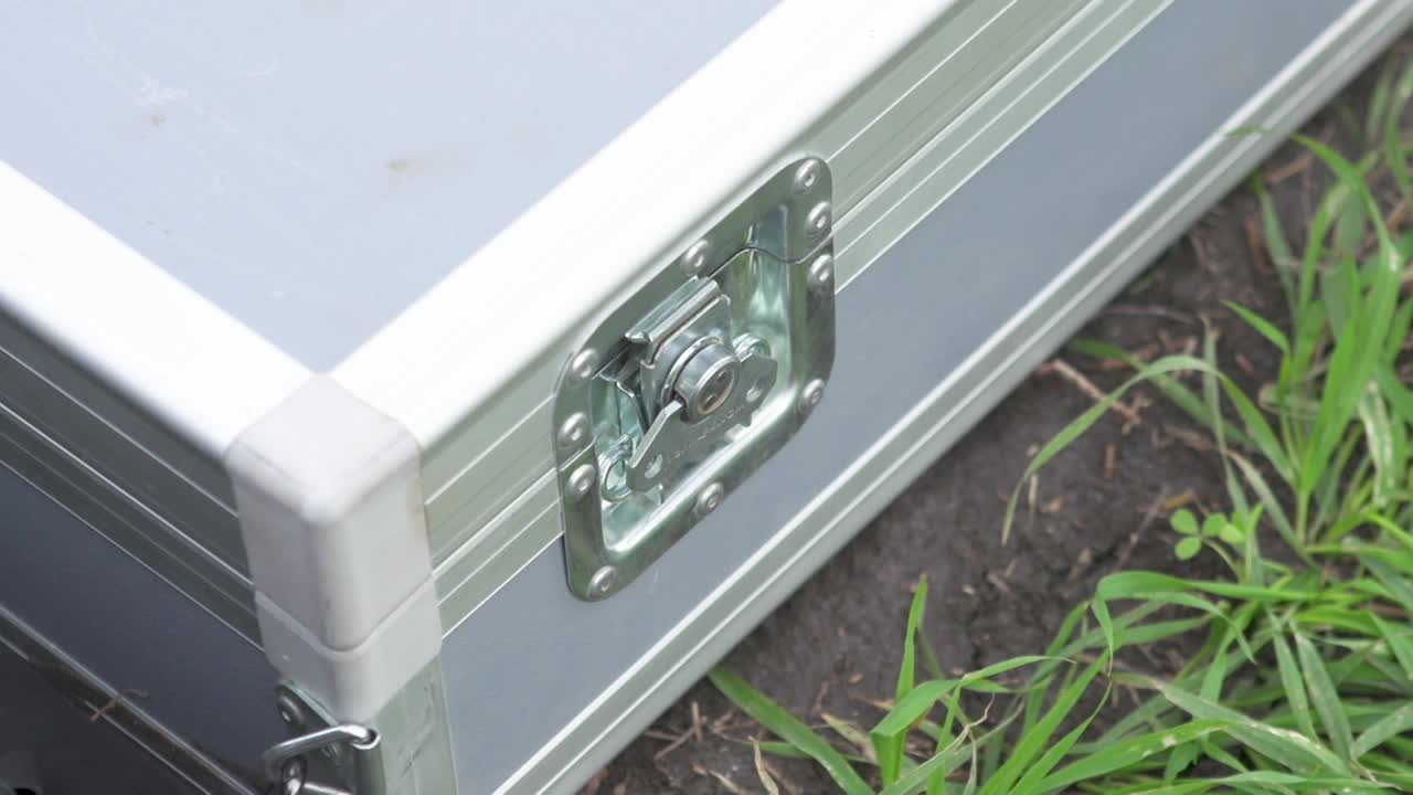 Close up of persons hand opens twist buckle on gray metal case on ground