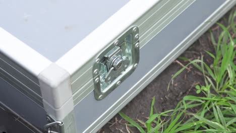 Close up of persons hand opens twist buckle on gray metal case on ground