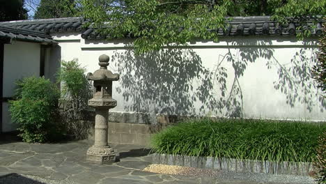 paved courtyard of a japanese garden with tiled wall and stone lantern