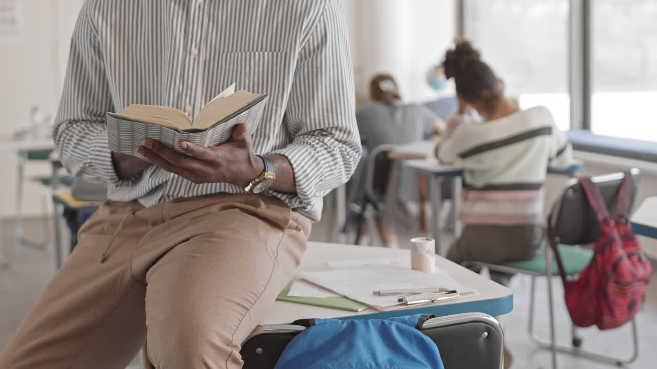 Midsection of Teacher Reading Book in Class