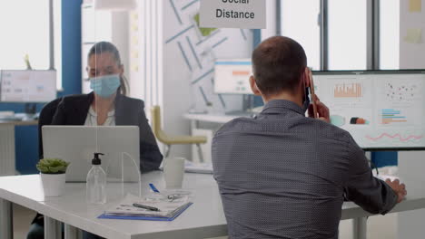 business man wearing face mask talking at phone while sitting at desk