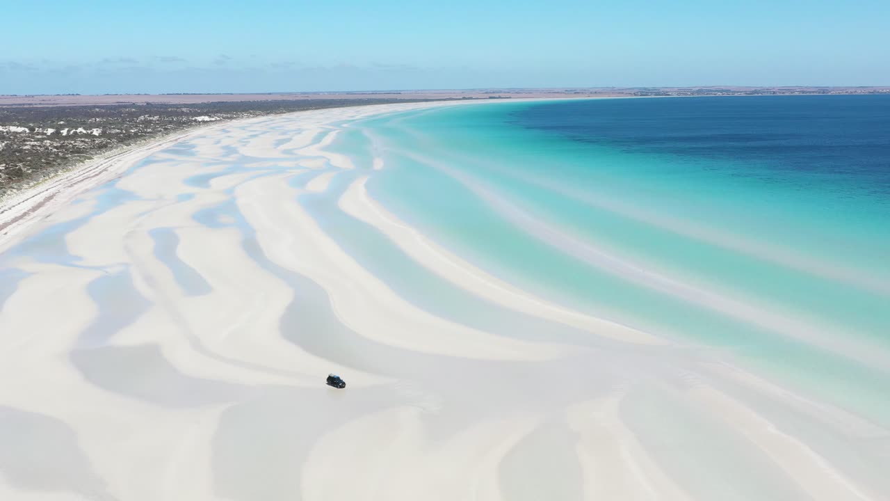 맑고 푸른 바닷물 근처의 플래허티 해변의 백사장에서 운전하는 밴의 훌륭한 항공 샷