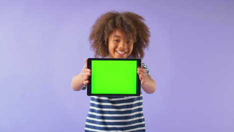 studio portrait of boy using digital tablet with green screen against purple background