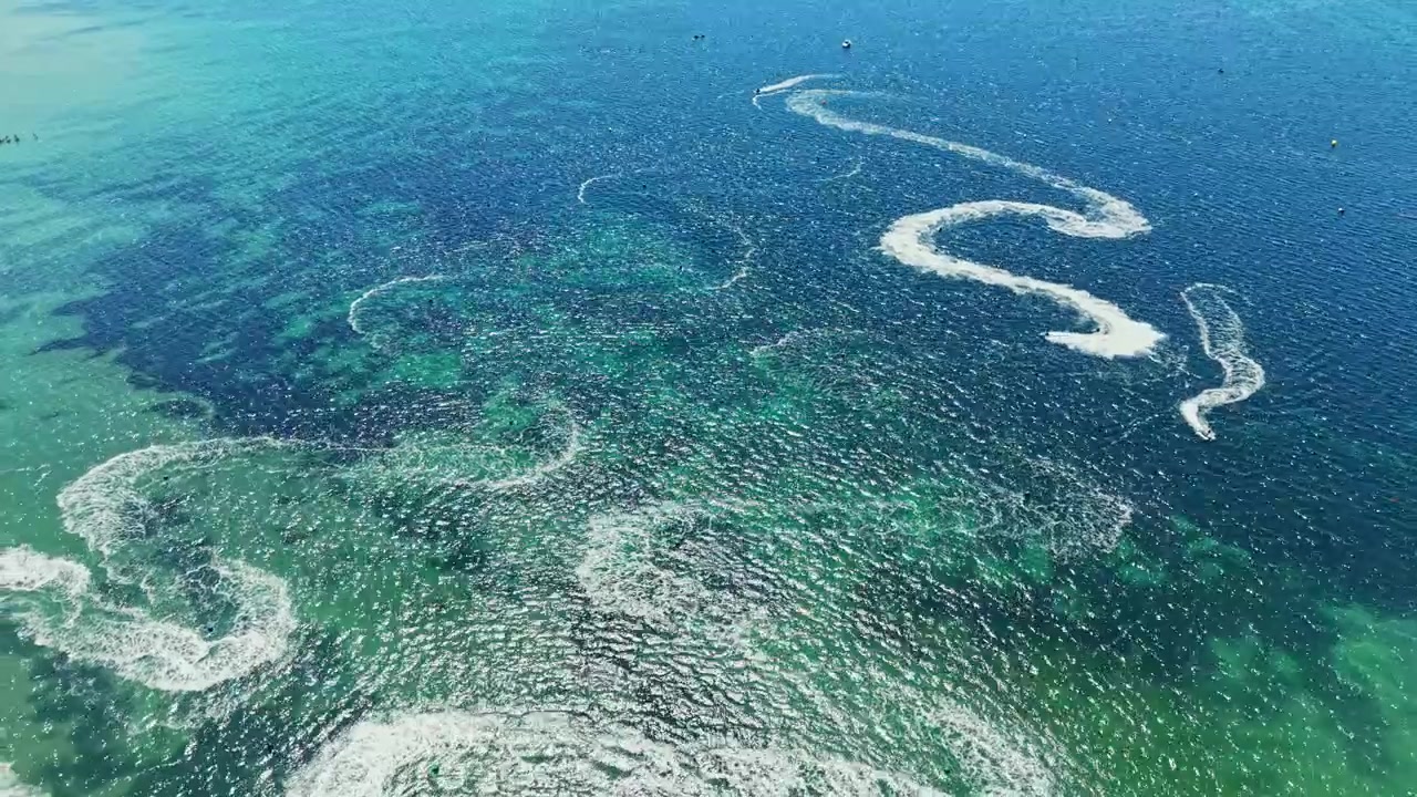 Jet ski racing takes place over clear blue water during a sunny day in a coastal area