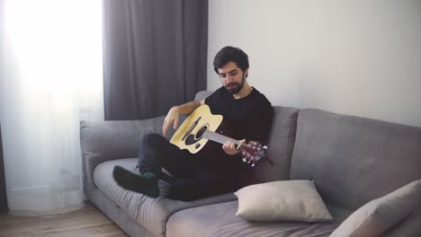 a young man sits on the couch and plays the guitar