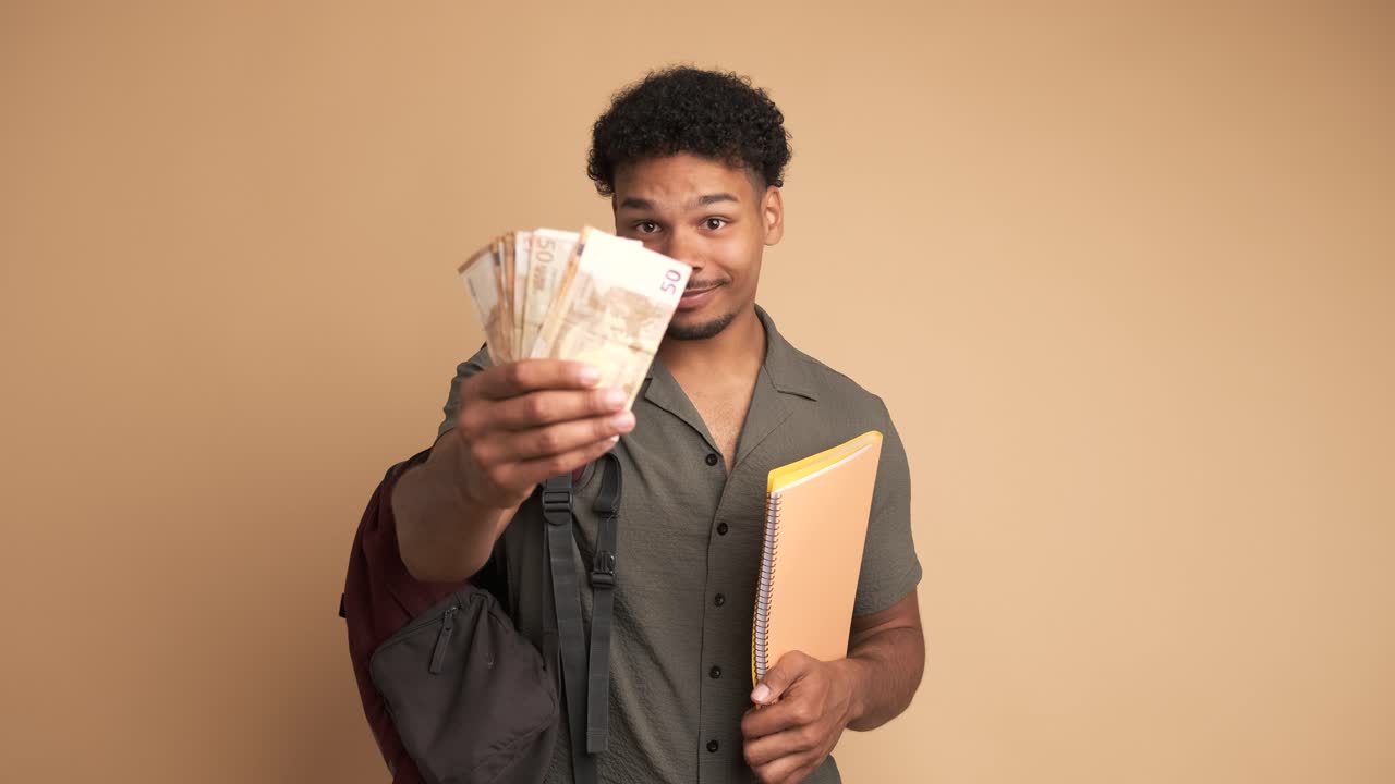 Happy young male student displaying scholarship money in beige studio