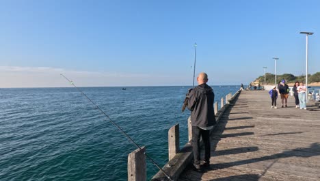 man fishing on pier, people walking