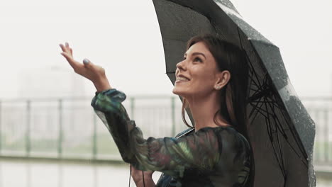 Happy-woman-with-black-umbrella-holds-palm-under-light-rain