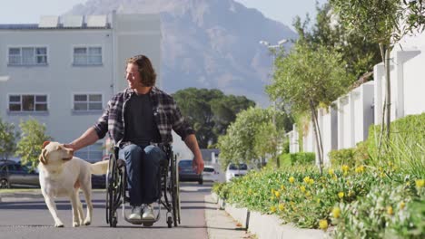 Smiling-caucasian-disabled-man-in-wheelchair-taking-his-pet-dog-for-a-walk-in-street